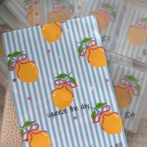 May include: A collection of clear plastic binder inserts and a binder cover with a lemon theme. The cover has blue and white stripes, yellow lemons, pink bows, and the phrase "squeeze the day".