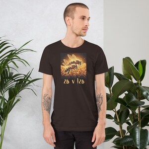 May include: A dark brown t-shirt featuring a graphic of two bees with glowing wings and a honeycomb background. The text "2B v !2B" is printed below the graphic. The shirt is made of a soft material.