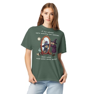 Könnte beinhalten: Grünes T-Shirt mit einer Illustration von zwei Hexen und einem Spiegel. Der Text auf dem Shirt lautet: "Wenn zwei Hexen zwei Uhren betrachten würden, welche Hexe würde welche Uhr betrachten?" Das Design ist auf dem Shirt zentriert.