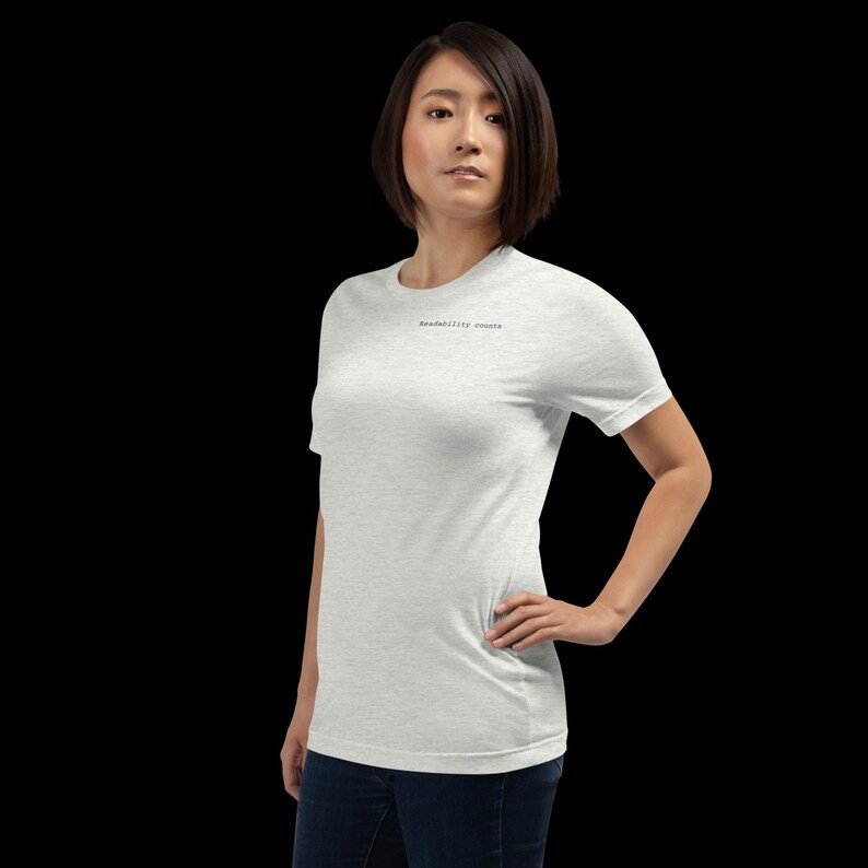 Op de afbeelding: Een lichtgrijs t-shirt met de tekst "readability counts" in een klein, zwart lettertype. Het shirt heeft korte mouwen en is gemaakt van een zacht materiaal. Het model draagt een blauwe jeans.