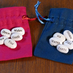 May include: Two small red and blue fabric bags with white beans inside. The beans are labeled with the words "Storm", "Water", "Earth", "Fire", and "Ice".