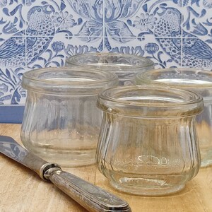 May include: Four clear glass jars with a ribbed design. The jars are empty and sitting on a wooden surface.