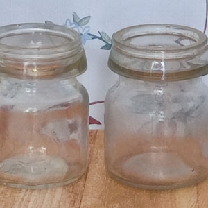 May include: Two clear glass jars with lids. The jars are empty and have a slightly cloudy appearance.