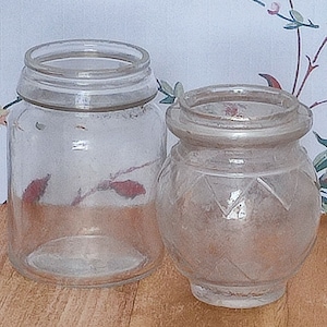 May include: Two clear glass jars, one with a smooth surface and the other with a textured diamond pattern. Both jars are empty.