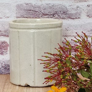 May include: A white ceramic planter with a ribbed design. The planter is sitting on a wooden surface with a bouquet of red and yellow flowers.