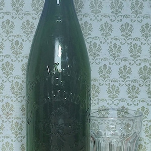 May include: A vintage green glass bottle with embossed lettering, alongside a clear, faceted glass. The bottle features a dark green cap and reads "H & G Diamonds Brewers Reading". The glass is a short tumbler.