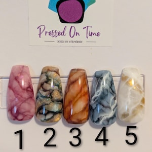 May include: A set of five press-on nails with marble designs in various colors. The nails are numbered 1 through 5. The top of the image has a logo that says "Pressed On Time" with a nail polish bottle graphic.