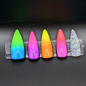 May include: Five ombre nail tips with a gradient of green to blue, pink to purple, orange to yellow, red to pink, and a clear nail tip with iridescent glitter.