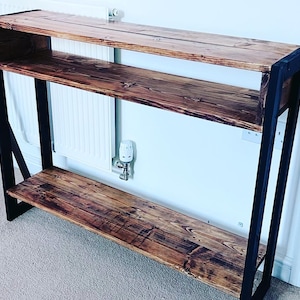 May include: A rustic wooden console table with two shelves and a black metal frame. The table has a distressed wood finish and is ideal for displaying decor or storing items.