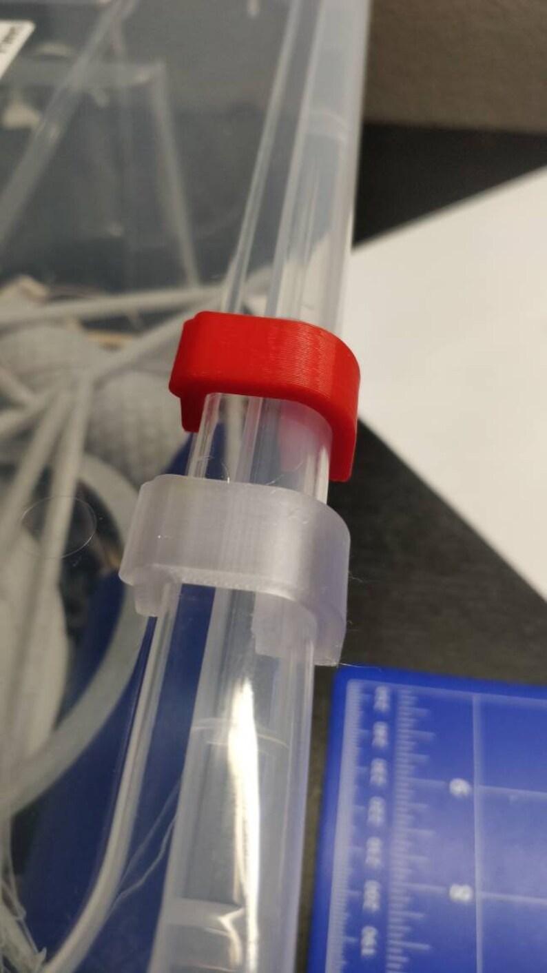 May include: A clear plastic storage container with a red plastic latch. The latch is attached to the side of the container and is used to secure the lid.