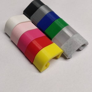 May include: A stack of colourful plastic pieces, each with a curved shape and a small hole. The colours are white, pink, red, yellow, green, blue, grey, and black.
