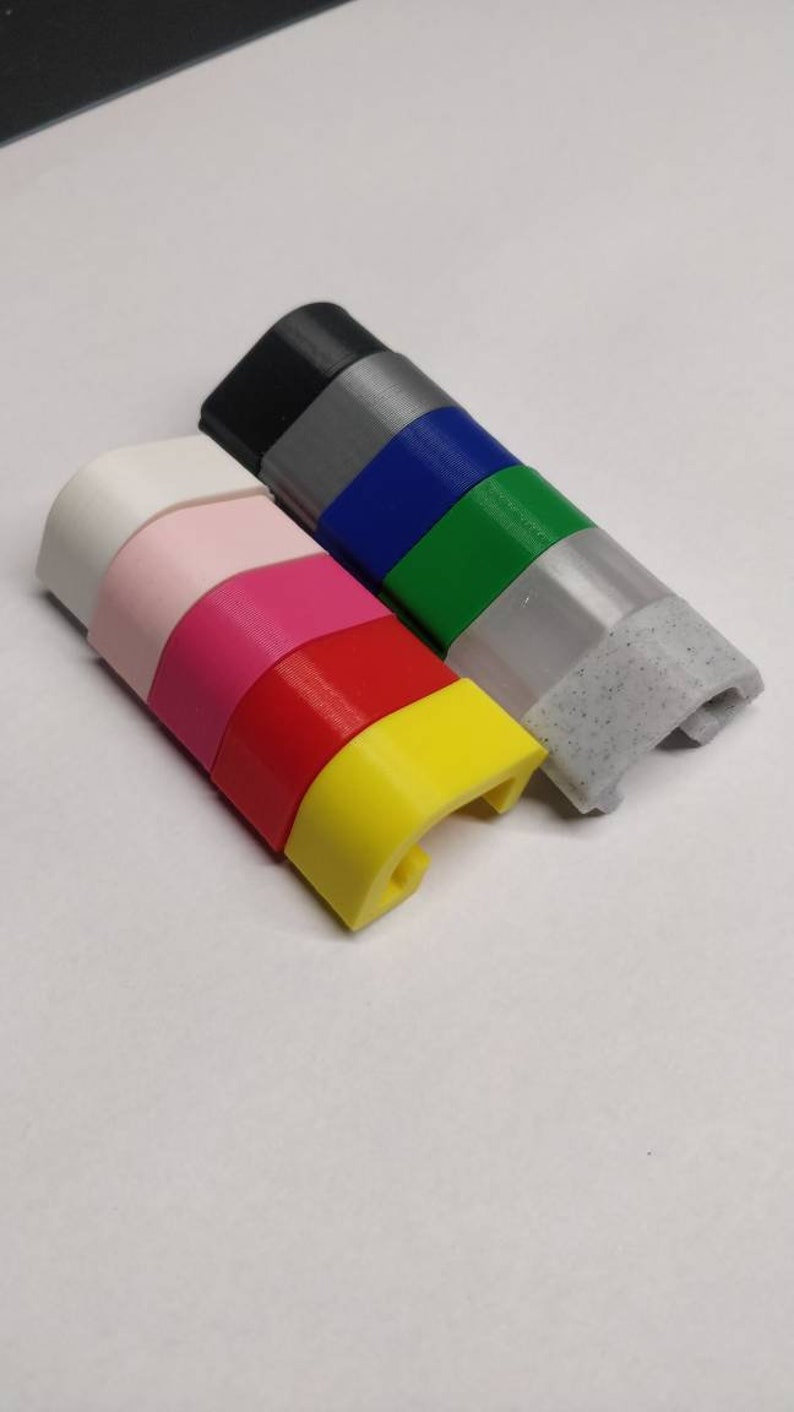 May include: A stack of colourful plastic pieces, each with a curved shape and a small hole. The colours are white, pink, red, yellow, green, blue, grey, and black.