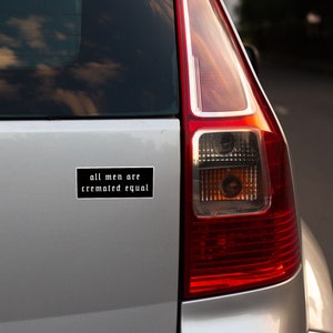 May include: A black and white bumper sticker with the text "all men are cremated equal" on a silver car.