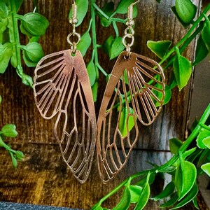 May include: Gold butterfly earrings with a delicate, intricate design. The earrings are made of metal and have a dangling style.