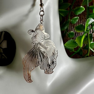May include: Gold-tone dangle earrings featuring a detailed cutout design of a fish with flowing fins.