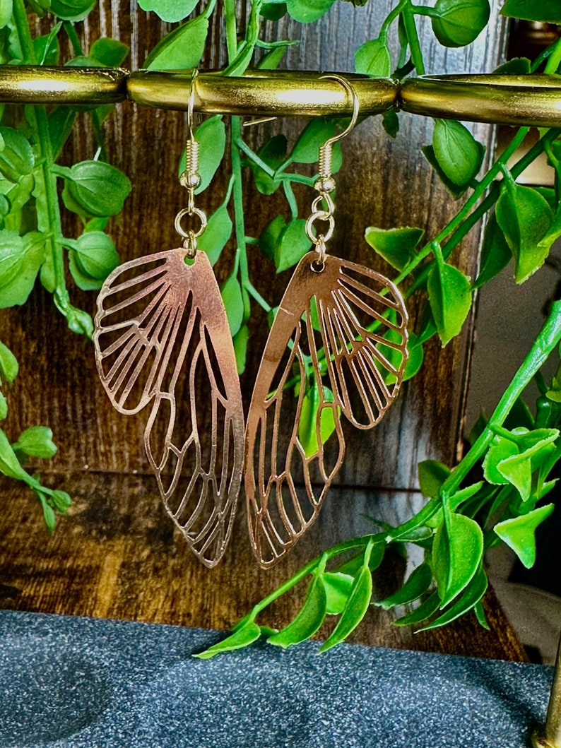 May include: Gold butterfly earrings with a delicate, intricate design. The earrings are made of metal and have a dangling style.
