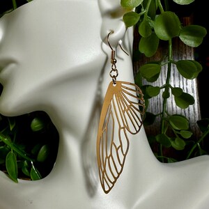 May include: Gold-toned butterfly wing earrings. The earrings are made of metal and have a delicate, intricate design.