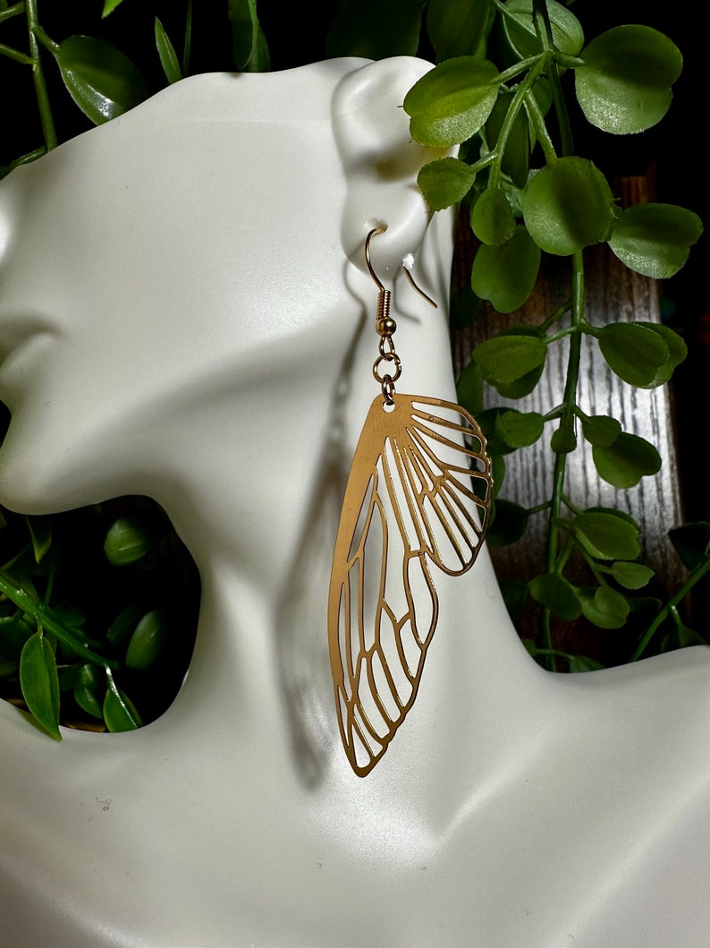 May include: Gold-toned butterfly wing earrings. The earrings are made of metal and have a delicate, intricate design.
