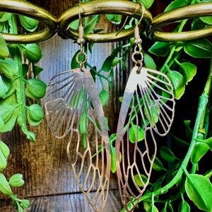 May include: A pair of gold-toned earrings shaped like butterfly wings. The earrings are hanging from a gold-toned chain.