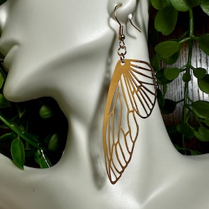 May include: Gold-toned butterfly-shaped earrings with a delicate, intricate design. The earrings are dangling and have a simple hook closure.