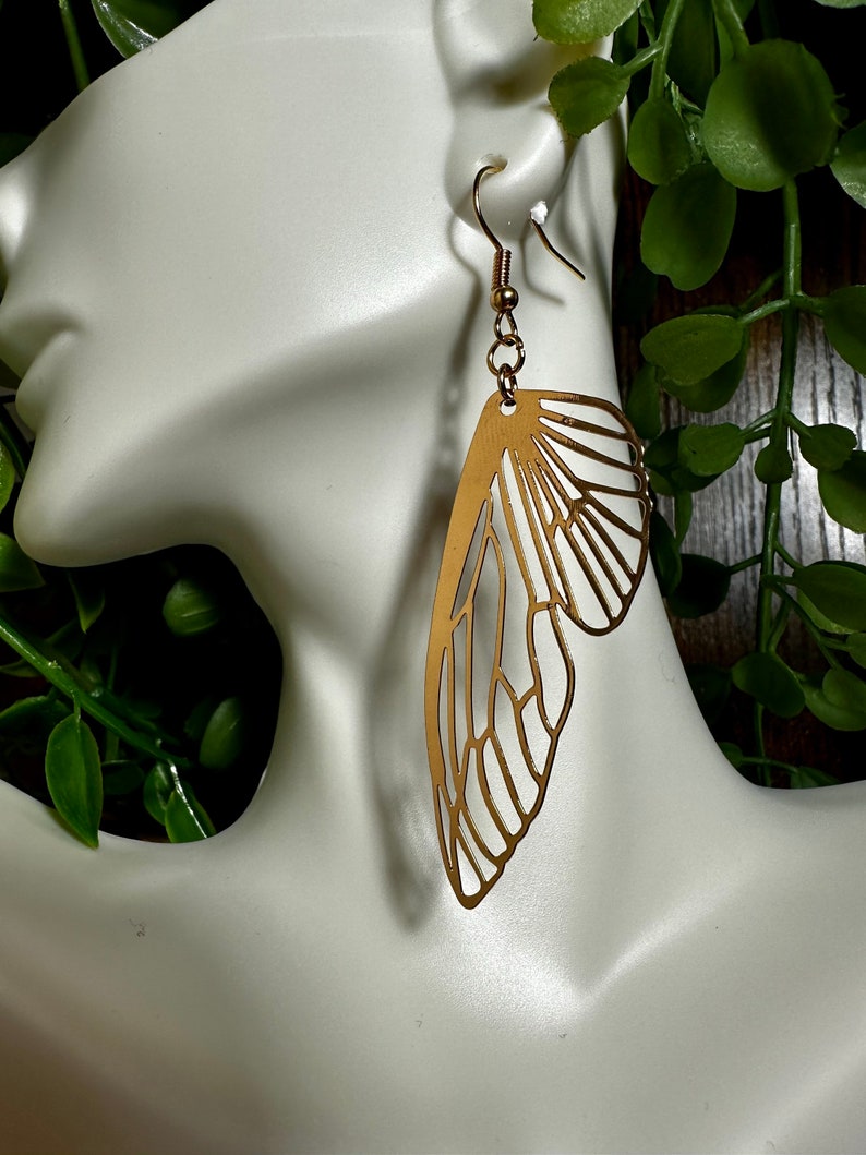May include: Gold-toned butterfly-shaped earrings with a delicate, intricate design. The earrings are dangling and have a simple hook closure.