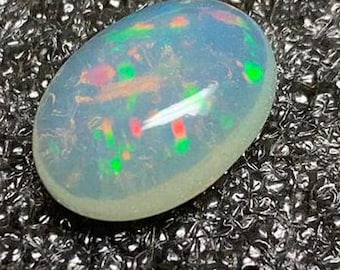 Puede incluir: Una piedra preciosa de ópalo ovalada blanca con destellos de color verde, rojo y rosa.