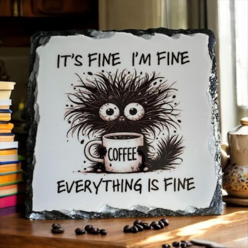 May include: A decorative slate sign with the text "IT'S FINE I'M FINE EVERYTHING IS FINE". The sign features a cartoon illustration of a black, furry creature with large eyes holding a coffee mug. The mug says "COFFEE".