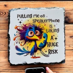May include: A decorative slate sign with a cartoon bird holding a phone, with the text "Putting me on speakerphone is taking a HUGE RISK." The sign is on a wooden surface.