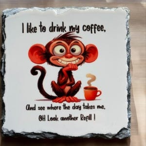 May include: A decorative stone tile with a cartoon monkey and coffee cup illustration. The text reads, "I like to drink my coffee, And see where the day takes me, OH Look another Refill!" The tile has a white background and a dark gray border.