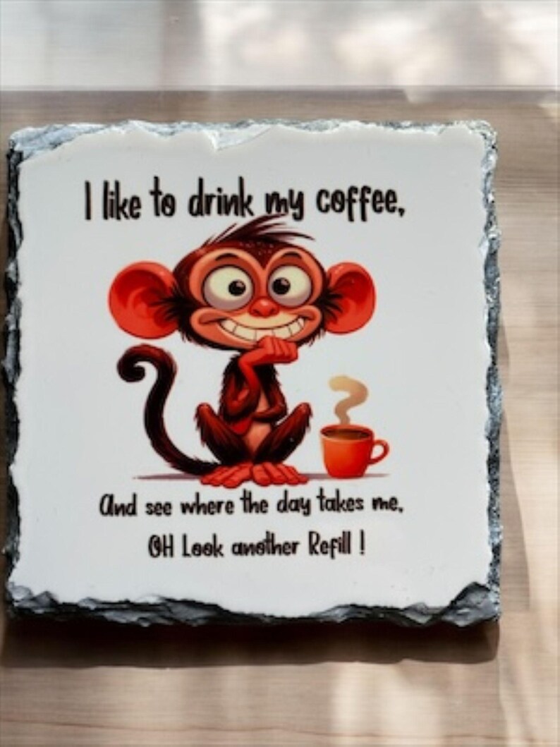 May include: A decorative stone tile with a cartoon monkey and coffee cup illustration. The text reads, "I like to drink my coffee, And see where the day takes me, OH Look another Refill!" The tile has a white background and a dark gray border.