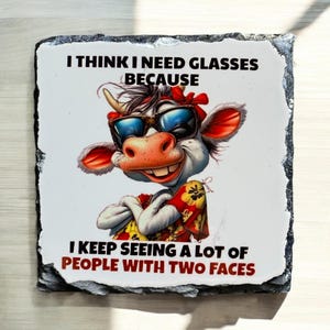 May include: A decorative square stone coaster featuring a cartoon cow wearing sunglasses and a red bandana. The text reads, "I THINK I NEED GLASSES BECAUSE I KEEP SEEING A LOT OF PEOPLE WITH TWO FACES."