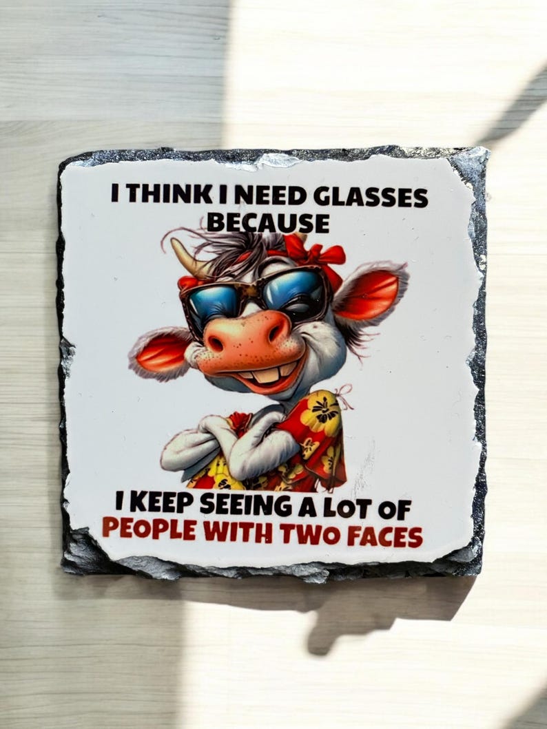 May include: A decorative square stone coaster featuring a cartoon cow wearing sunglasses and a red bandana. The text reads, "I THINK I NEED GLASSES BECAUSE I KEEP SEEING A LOT OF PEOPLE WITH TWO FACES."