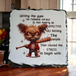 May include: A decorative stone plaque with a humorous illustration of a cartoon dog holding a baseball bat. The text reads "Hitting the gym to release stress is not nearly as EFFECTIVE as hitting the people that caused the STRESS to begin with."