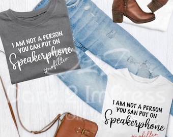 May include: Two t-shirts with the text "I am not a person you can put on speakerphone #nofilter" printed on them. The shirts are folded and laid out on a white surface with a pair of brown boots and a brown leather bag.