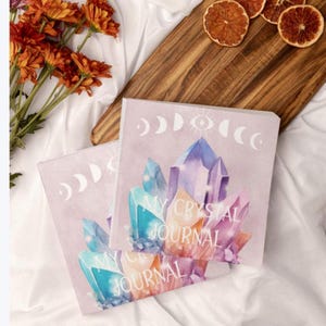May include: Two pastel pink journals with watercolor illustrations of crystals and the text "My Crystal Journal". The journals have a moon and eye design on the cover.