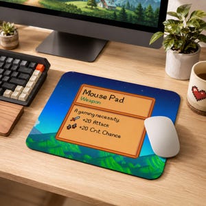 Puede incluir: Una alfombrilla de ratón rectangular con un paisaje de arte píxel y un cuadro de descripción color canela. El texto dice: Mouse Pad, Weapon, A gaming necessity, +20 Attack, +20 Crit. Chance. El fondo muestra un cielo azul y colinas verdes.
