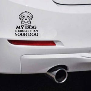 Puede incluir: Adhesivo para coche en blanco y negro con una ilustración de perro y el texto "MY DOG IS COOLER THAN YOUR DOG". El adhesivo está en un parachoques blanco, con un reflector rojo y un tubo de escape visibles.