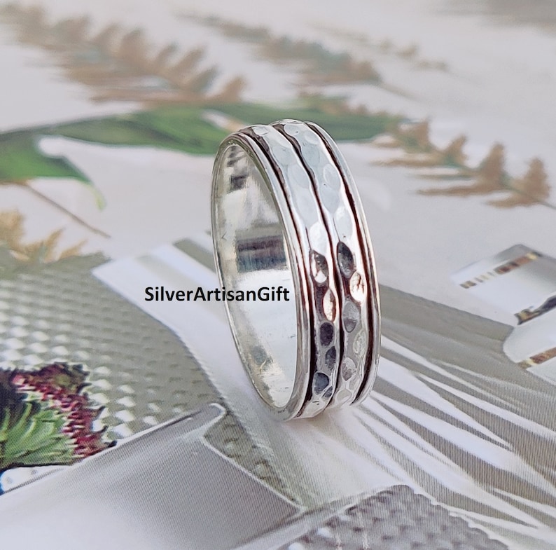 May include: A silver spinning ring with a hammered texture. The ring has three bands that spin freely.