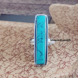 May include: A silver ring featuring a turquoise stone set in a rectangular shape. The stone has a marbled pattern and is a vibrant blue-green colour.