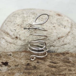 Peut inclure: Boucle d'oreille en argent avec un design en spirale. La boucle d'oreille est faite d'un seul fil de métal tordu et façonné en spirale. La boucle d'oreille est ouverte en haut et en bas, ce qui permet de la mettre et de l'enlever facilement de l'oreille.