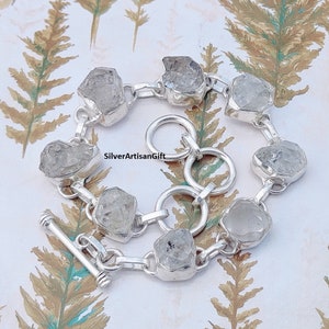 May include: A silver bracelet with a toggle clasp features faceted clear quartz stones. The bracelet is made of sterling silver and has a polished finish.  SilverArtisanGift is printed on the bracelet.