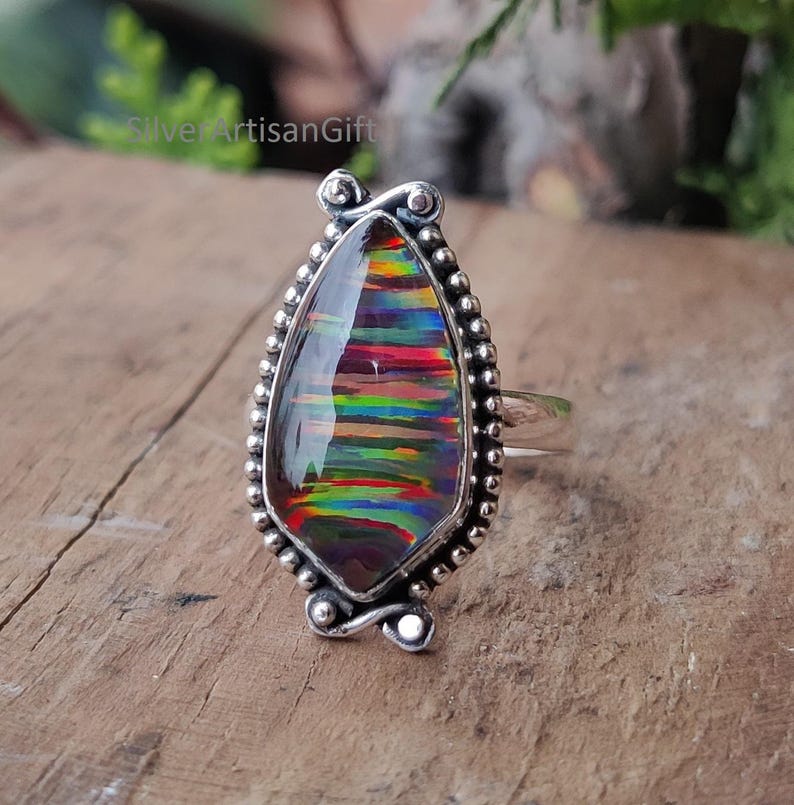 Puede incluir: Un anillo de plata con una gran &oacute;palo en forma de l&aacute;grima. El &oacute;palo muestra una vibrante gama de colores, incluyendo rojo, verde y azul, con un patr&oacute;n de rayas. El anillo tiene un borde detallado con cuentas y detalles decorativos.