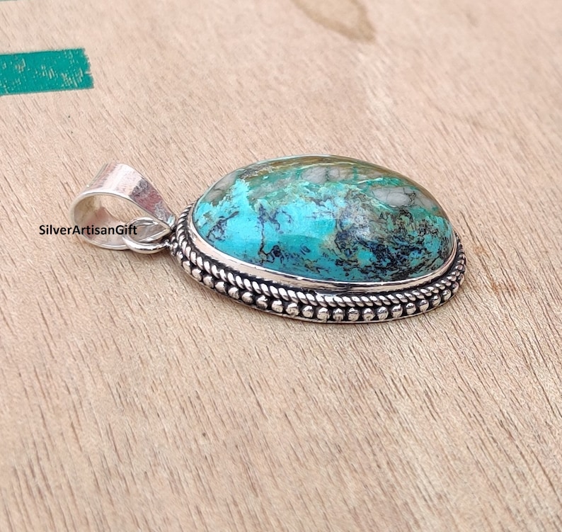 May include: A turquoise gemstone pendant with a silver setting. The pendant has a rope-like border and a silver bail.