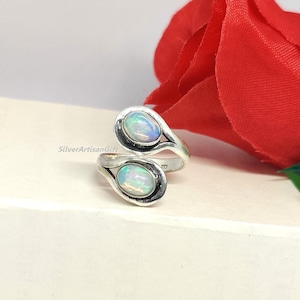 Könnte beinhalten: Ein silberner Ring mit zwei ovalen Opalen. Der Ring ist so konzipiert, dass er sich um den Finger wickelt.