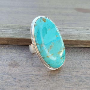 May include: A turquoise oval ring set in sterling silver. The turquoise is a vibrant blue-green color with brown matrix.