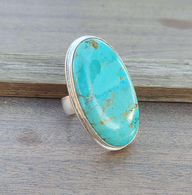 May include: A turquoise oval ring set in sterling silver. The turquoise is a vibrant blue-green color with brown matrix.