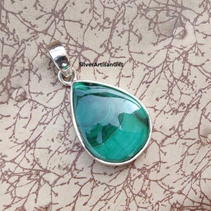 May include: A teardrop-shaped pendant with a polished, vibrant green malachite stone set in a silver bezel. The stone displays natural swirling patterns. The pendant has a silver bail for attaching to a chain. The text "SilverArtisanGift" is visible.