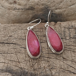 May include: A pair of silver earrings with teardrop-shaped red gemstones. The earrings have a simple design and are perfect for everyday wear.