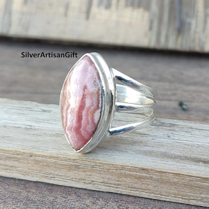 May include: A silver ring featuring a pink and white marbled gemstone. The ring has a delicate, three-pronged band.