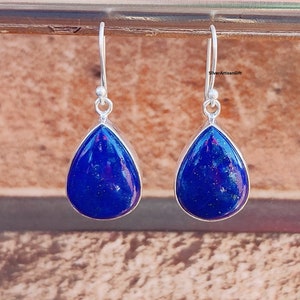以下が含まれることがあります： 青いラピスラズリ石が付いた、シルバーの涙型のイヤリングのペア。イヤリングはシンプルなデザインで、普段使いに最適です。
